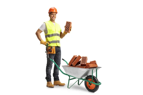 Construction Worker Holding Brick Standing Wheelbarrow Pile Bricks Isolated White — Stock Photo, Image