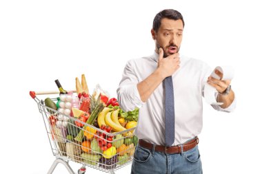 Alışveriş arabasıyla şok olmuş bir adam beyaz arka planda izole edilmiş bir faturayı kontrol ediyor.