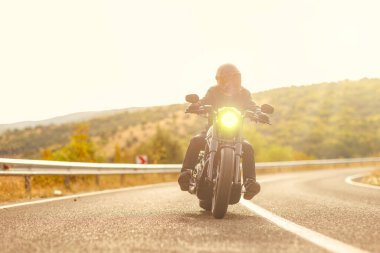 Gün batımında açık bir yolda motosiklet süren kasklı bir adam.