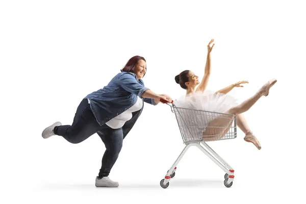 一个肥胖的女人把芭蕾舞演员推进一辆白色背景的购物车 — 图库照片