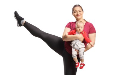 Anne egzersiz yapıyor, bacağını kaldırıyor ve beyaz arka planda izole edilmiş bir bebeği tutuyor.