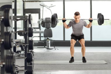 Spor salonunda ağırlık kaldıran bir adamın tam boy portresi.