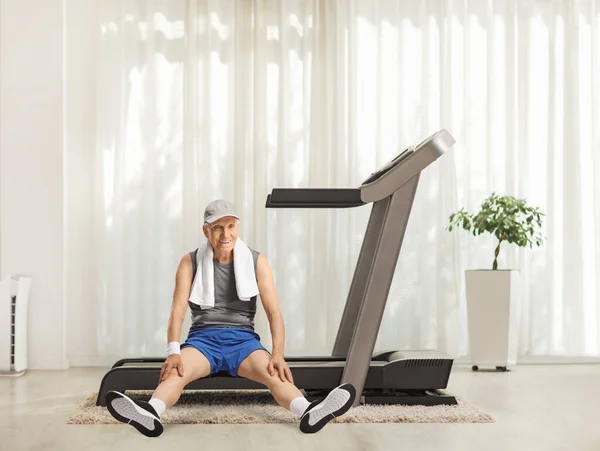 Tired elderly man sitting on a treadmill at home and smiling