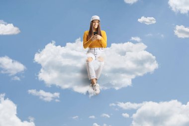 Genç bir kadın bulutların üzerinde yüzüyor ve gökyüzünde bir cep telefonuyla yazı yazıyor.