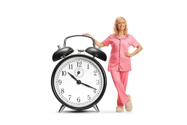 パジャマの女性は 大きな目覚まし時計に漏れ 白い背景で孤立した微笑み — ストック写真