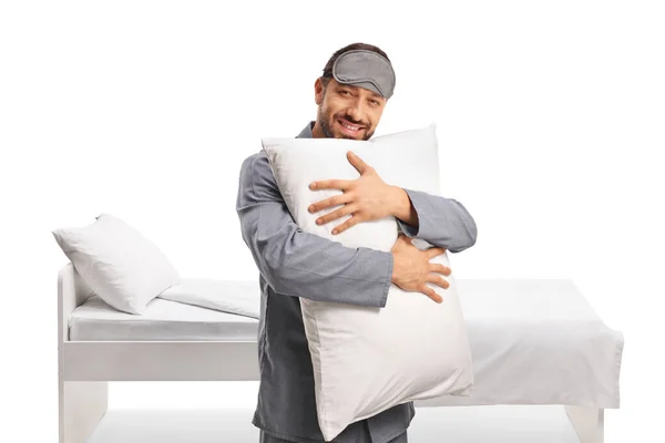 白い背景に隔離されたベッドの前に枕を抱擁する睡眠マスクとパジャマの幸せな男 — ストック写真