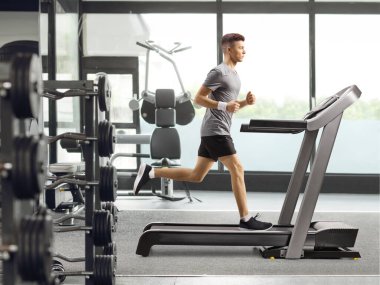 Spor salonunda koşu bandında antrenman yapan bir adamın tam boy profil fotoğrafı.