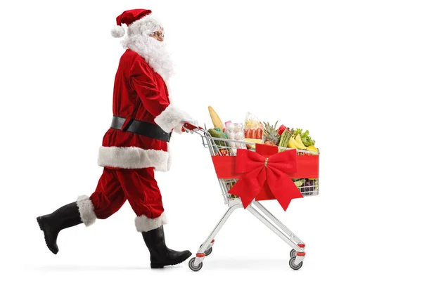 サンタクロースが走り 白い背景に隔離された赤い弓で結ばれた食べ物とショッピングカートを押す — ストック写真