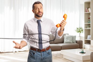 Evdeki bir oturma odasında telefon kablosuyla bağlanmış sinirli genç bir adam.
