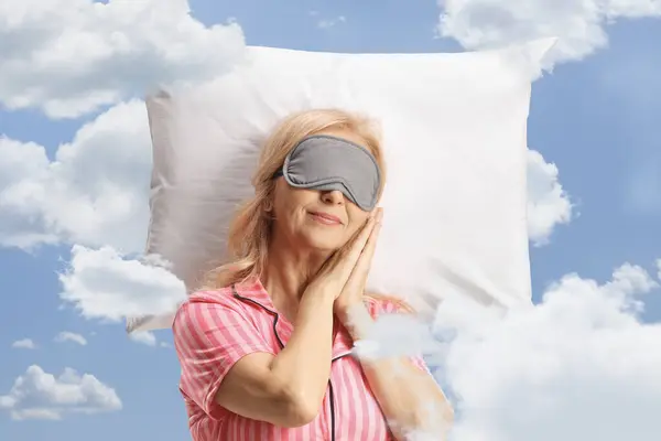 Mature woman with a mask sleeping peacfully on a pillow in the sky with clouds around