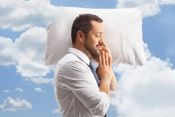 Profile shot of a businessman sleeping on a pillow in a shirt and tie with clouds and blue sky around
