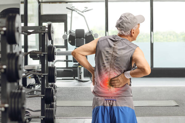 Rear view shot of an elderly man holding his back with visible spine bone at a gym