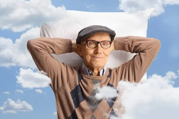 Happy elderly man resting on a pillow between clouds and blue sky