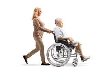 Beyaz arka planda, tekerlekli sandalyede yürüyen ve erkek bir hastayı iten bir kadının tam boy profil fotoğrafı.