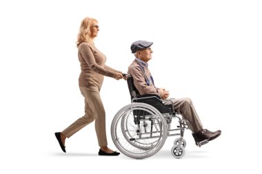 Beyaz arka planda sakat ve tekerlekli sandalyeli yaşlı bir adamı iten bir kadının tam boy profil fotoğrafı.