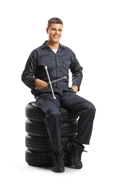 汽车修理工坐在一堆轮胎上 手里拿着一把用白色底座隔开的扳手工具 — 图库照片
