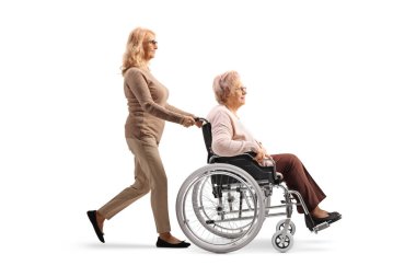 Beyaz arka planda, tekerlekli sandalyedeki yaşlı bir kadını iten bir kadının tam boy profil fotoğrafı.