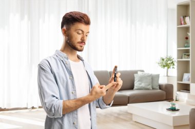 Adamın biri evde oturma odasında mızrak iğnesiyle parmağını dürtüyor.