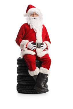 Noel Baba beyaz arka planda izole edilmiş lastik yığınının üzerinde oturuyor.