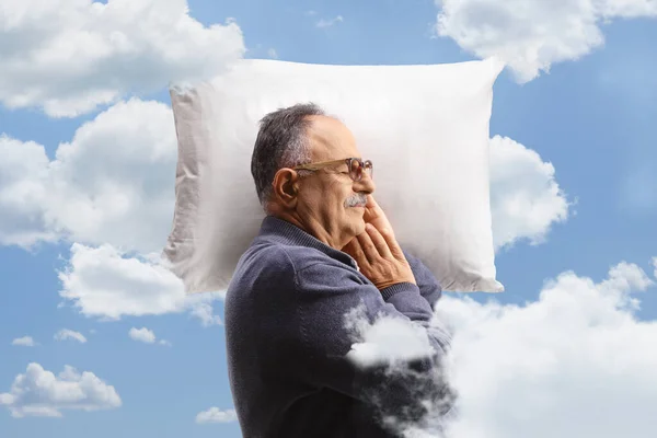 Profile shot of a mature man sleeping on a pillow between clouds on a blue sky