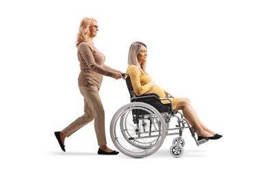 Olgun bir kadının beyaz arka planda izole edilmiş tekerlekli sandalyeli hamile bir kadını iterken tam boy profil fotoğrafı.