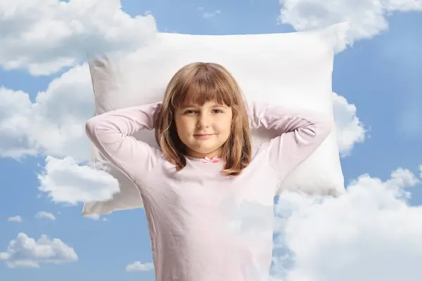 Sleepy girl in pajamas resting on a pillow up in the sky with clouds around