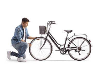 Diz çöküp bisiklet tekerleğini kontrol eden genç adam beyaz arka planda izole edilmiş.