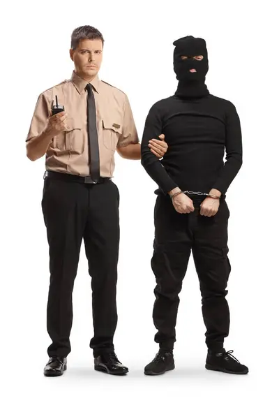 一名警卫站在一名身穿黑色衣服 头戴巴拉克拉瓦的窃贼身旁 背景为白色 全长画像 — 图库照片
