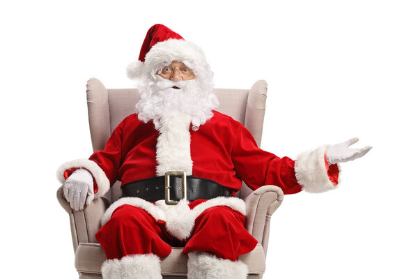 Santa claus seated in an armchair and showing something with hand isolated on white background