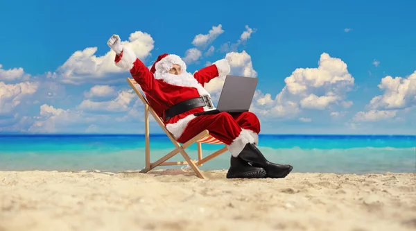海滩上的圣诞老人 坐在甲板上的椅子上 带着笔记本电脑 给人一种幸福的感觉 — 图库照片