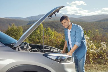 Genç adam yolda bir aracın motorunu kontrol ediyor.