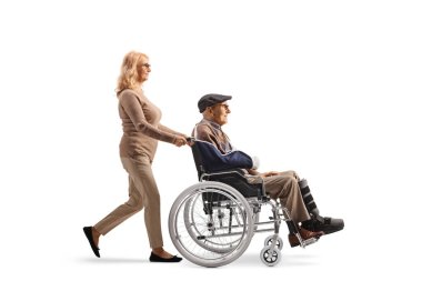 Beyaz arka planda, tekerlekli sandalyedeki yaşlı bir adamı iten olgun bir kadın.