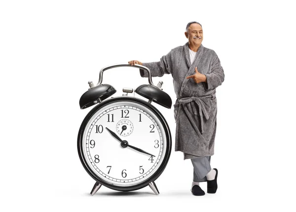 白い背景に隔離された大きな目覚まし時計を指すバスローブの成熟した男 — ストック写真