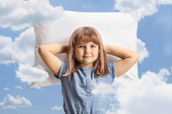 Cute little girl resting on a pillow among clouds on a blue sky