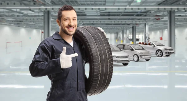 Worker holding a tire and pointing at a car manufacturing plant