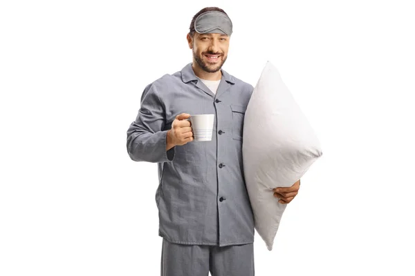 枕とホットドリンクを白い背景に隔離した睡眠マスクを持つパジャマの男 — ストック写真