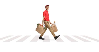 Paket taşıyan bir teslimatçının beyaz arka planda izole edilmiş bir caddeyi geçerken tam boy görüntüsü.