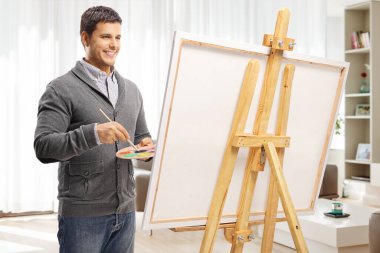 Evdeki tuvale resim yapan yakışıklı genç bir adam.