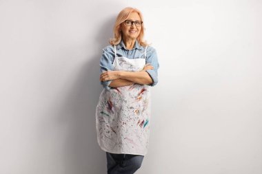 Beyaz önlüklü, boyalı ve duvara yaslanmış bir kadın.