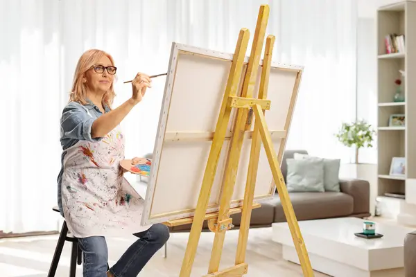 Woman holding a painting brush and palette with acrylic paint and painting at home