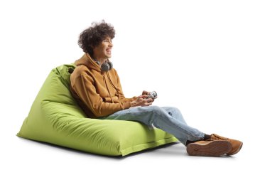 Yeşil fasulye çuvalında oturan ve beyaz arka planda izole edilmiş joystick ile oyun oynayan adam.
