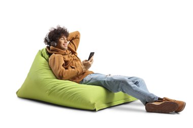 Fasulye sırığında oturan, kulaklıklı ve akıllı telefonlu beyaz arka planda izole edilmiş müzik dinleyen kıvırcık saçlı bir adam.