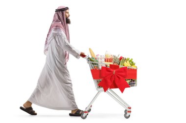 Beyaz arka planda kırmızı kurdeleli bir alışveriş arabasıyla yürüyen bir Arap 'ın tam boy profil fotoğrafı.