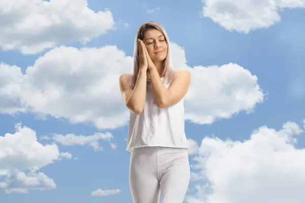Young woman in pajamas sleeping with clouds and sky in the background