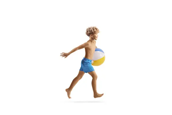 穿着泳裤的男孩带着一个被白色背景隔开的海滩球跑步 — 图库照片