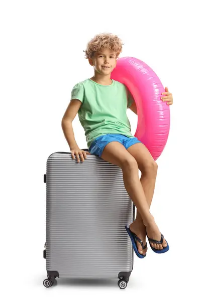 白い背景に隔離された夏休みのために詰まったスーツケースに座っているスイミングリングを持つ少年 — ストック写真