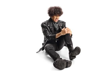 Deri ceketli, yaralı, yerde oturan ve dizini beyaz arka planda tutan genç adam.