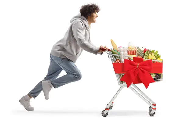 一个年轻的男人开着一辆白色背景的购物车 带着圣诞食品跑步 — 图库照片