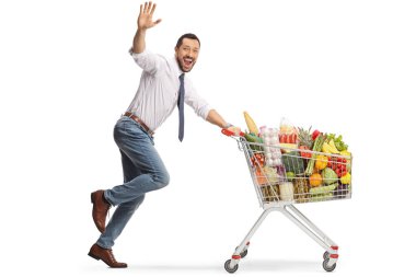 Neşeli bir adam alışveriş arabasıyla koşuyor ve beyaz arka planda izole edilmiş kameraya el sallıyor.