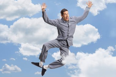 Young happy man in pajamas jumping high among clouds